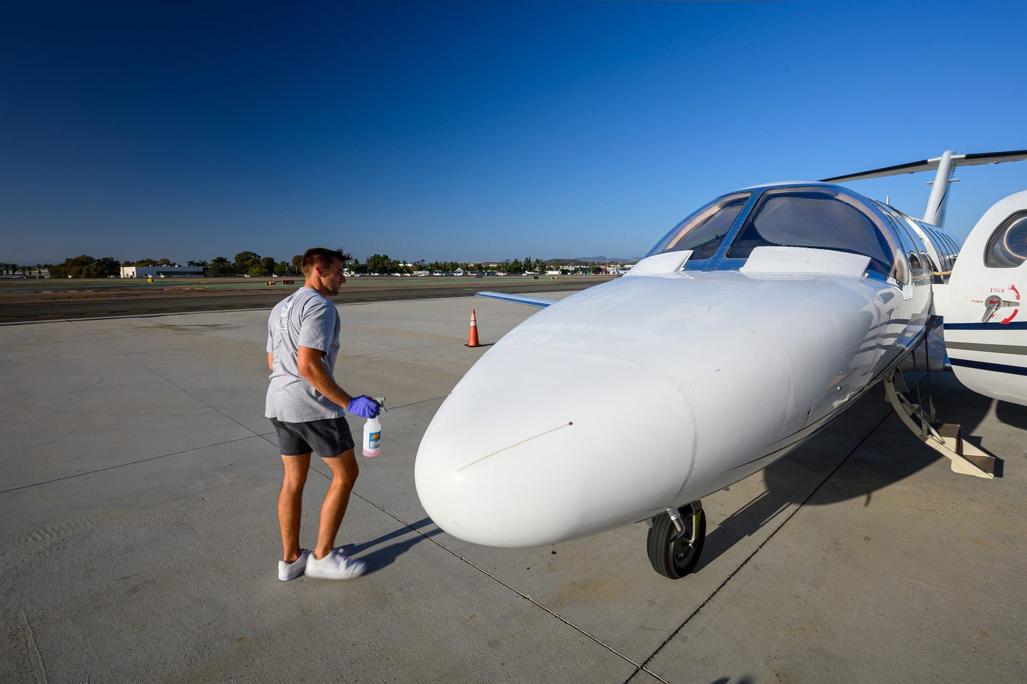 A detailer stands at the nose of a Citation jet with a spray bottle and microfiber cloth