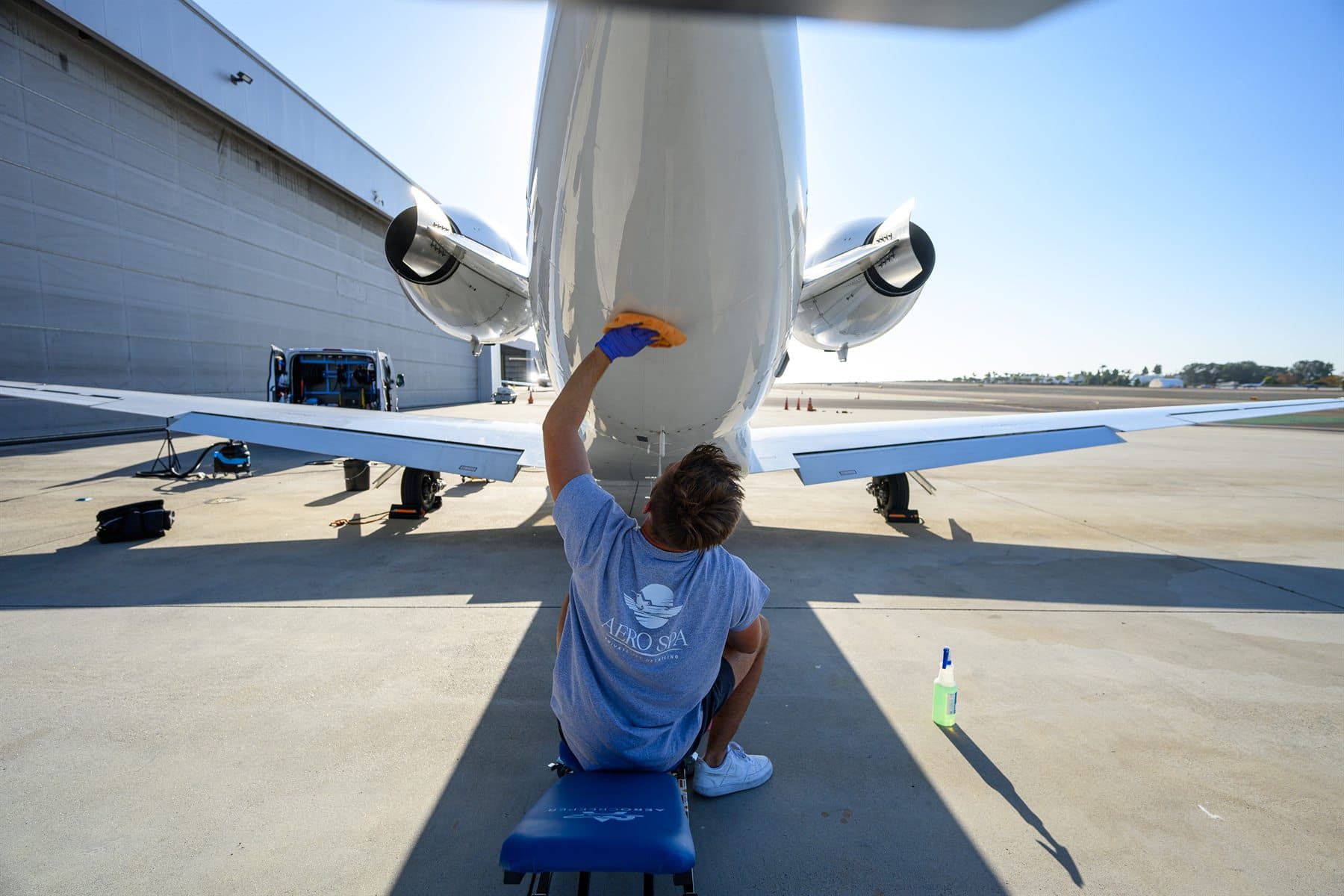 A detailer sits under the tail and wipes the belly of the jet by hand