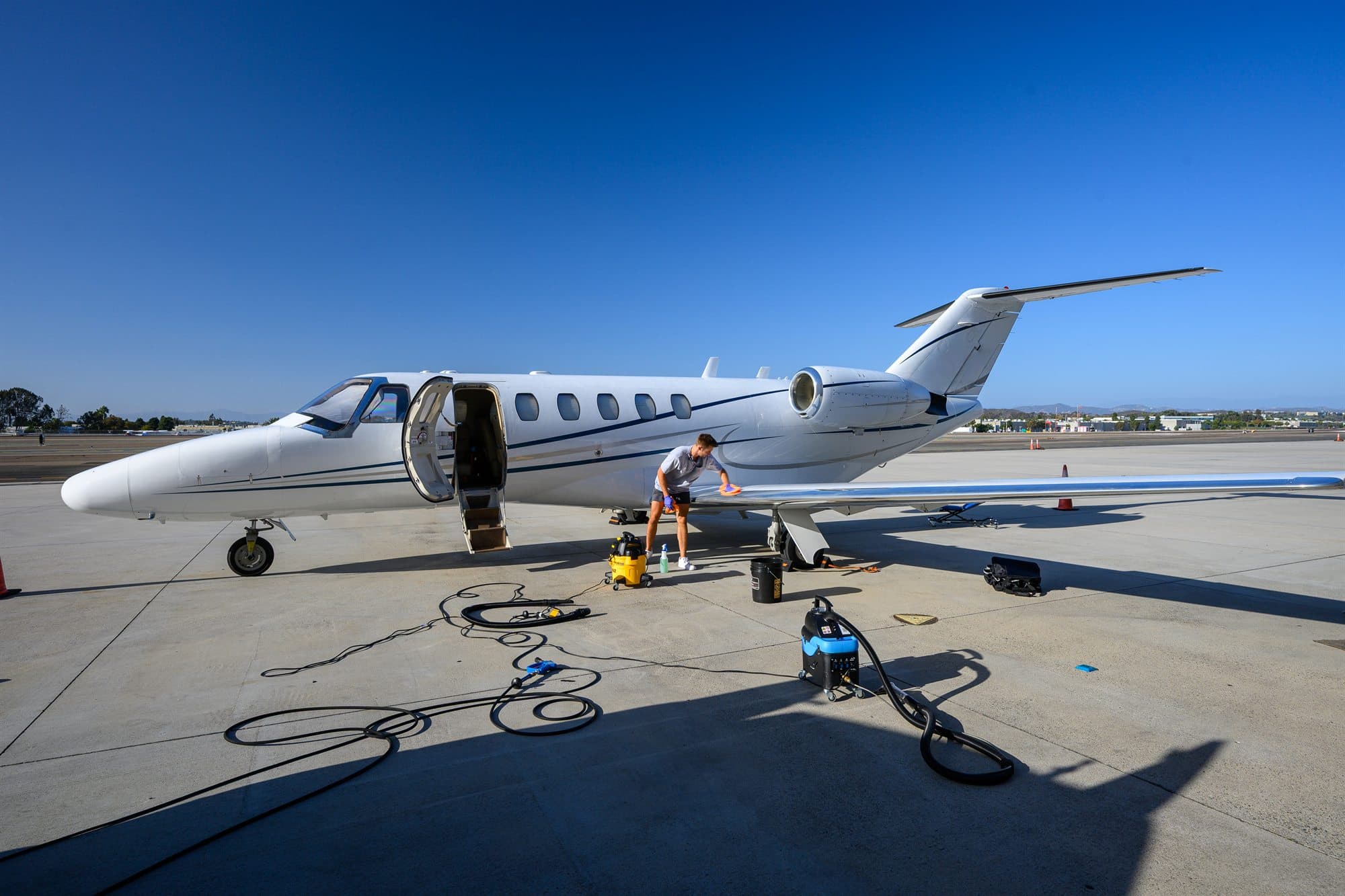 A detailer wipes the leading edge of the wing, with extractors, hoses and supplies laid out on the ramp